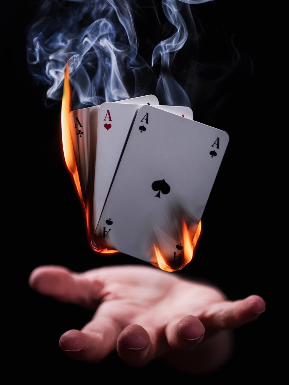 Four aces, including the Ace of Spades and Ace of Hearts, burn above an open hand with smoke rising.