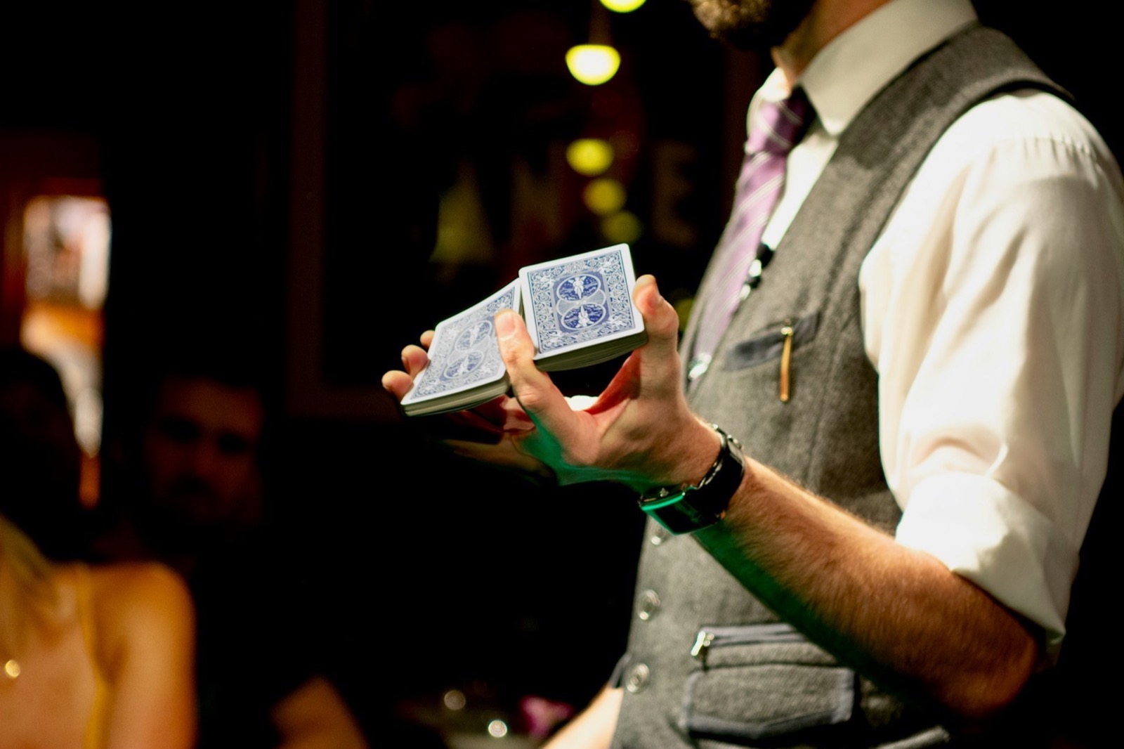Magician in a vest and tie shuffles a deck of playing cards in his hands.