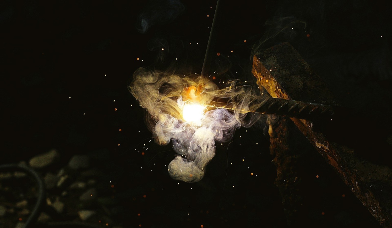 Bright welding arc creating sparks and smoke on a dark metal surface.