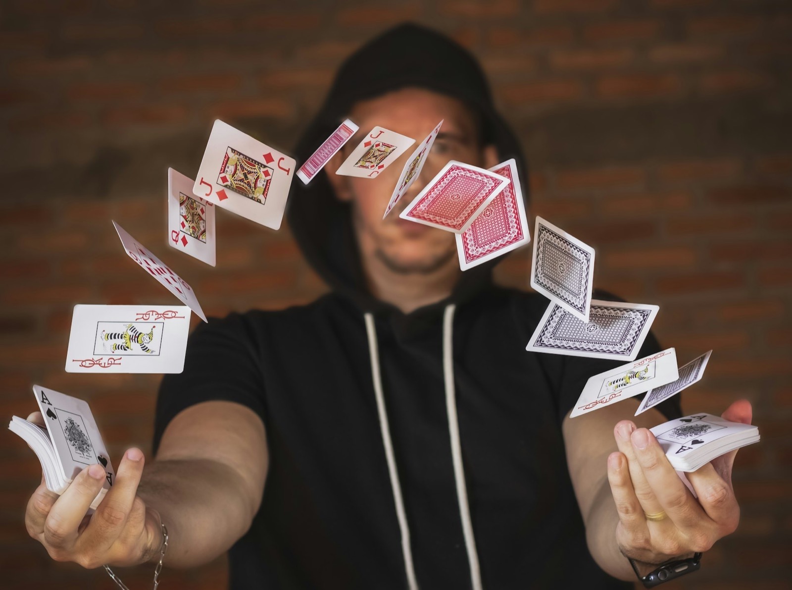 A magician in a black hoodie makes playing cards float and fly around him.