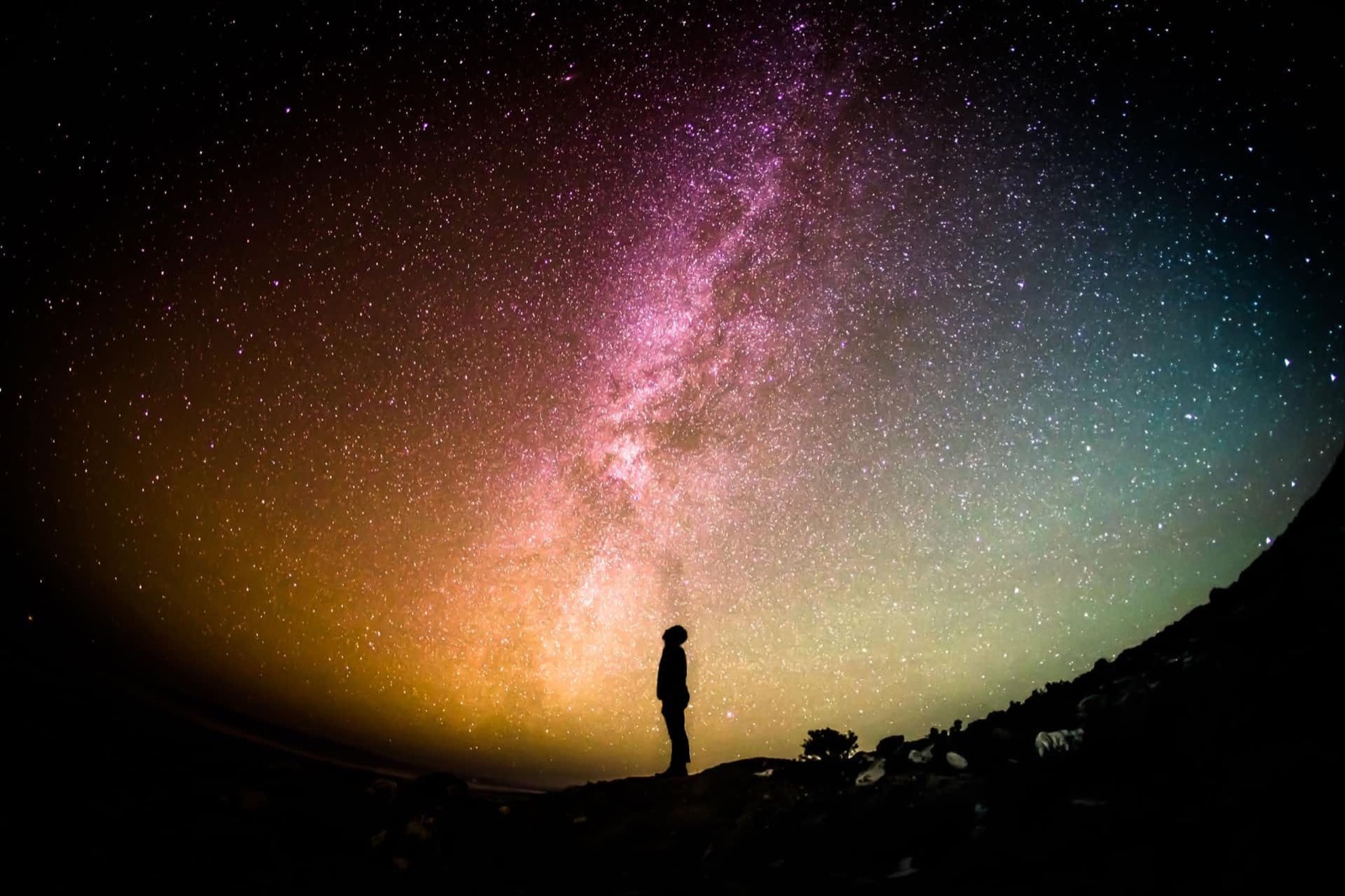 Person silhouetted against a vibrant, star-filled Milky Way galaxy.